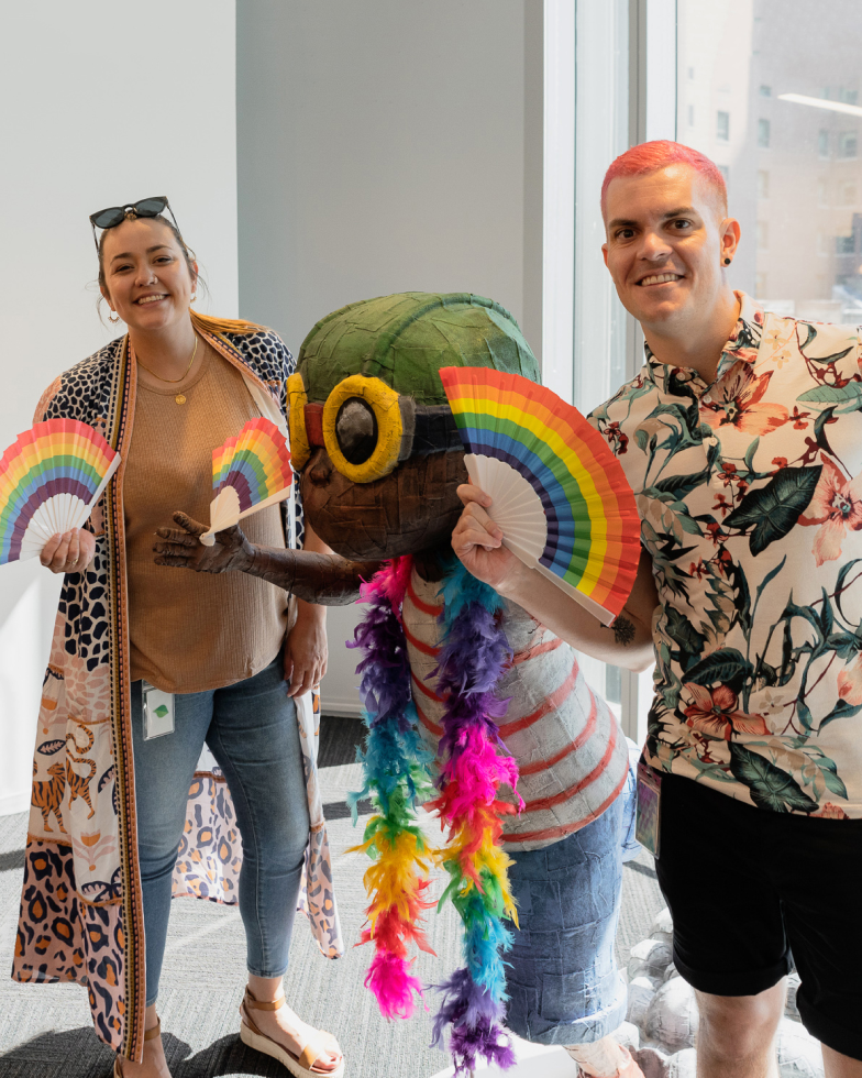 Two LGBTQIA at Sprout allies posing with an office statue decked out in pride gear.