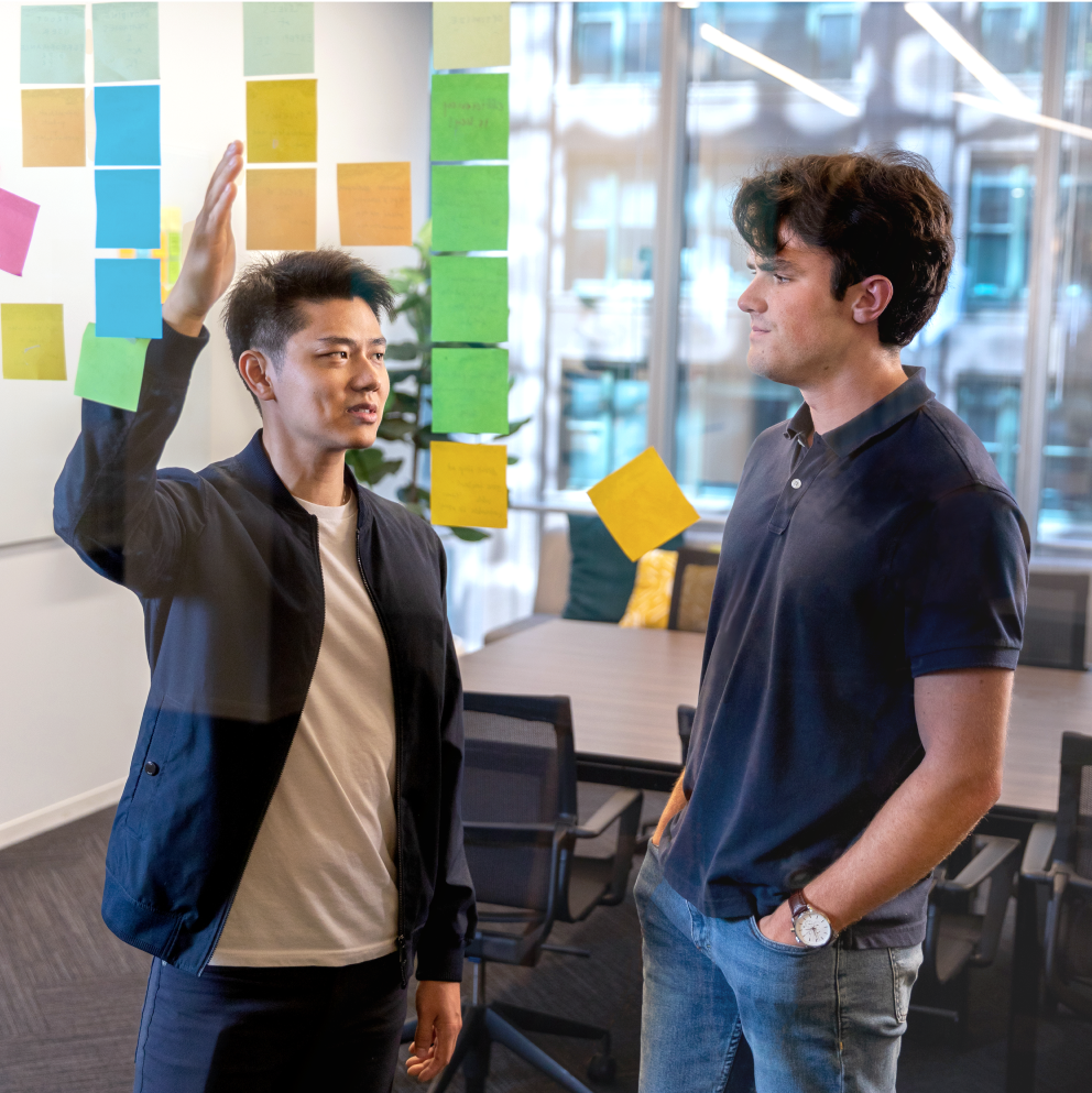 Two engineers problem-solving with sticky notes on a conference room wall