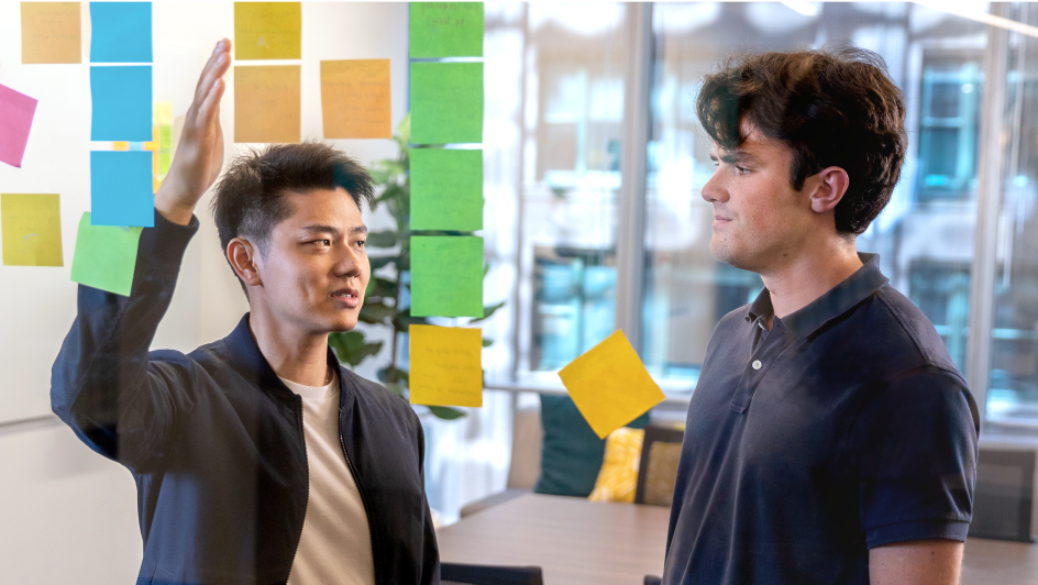 Two engineers problem-solving with sticky notes on a conference room wall