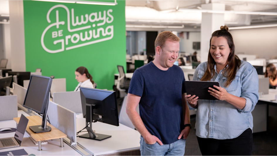 Two team members reviewing a contract together in front of our Always Be Growing in-office mural. 