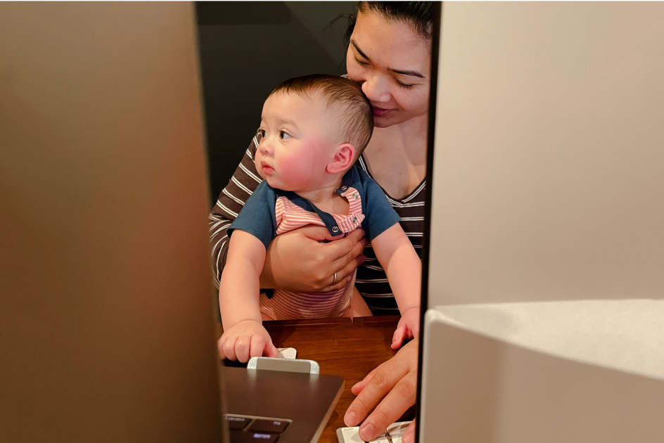 A female-identifying Sprout employee holding her small child while working on her laptop.