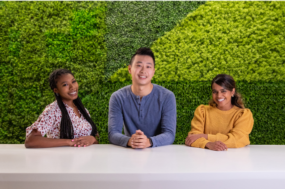 Racially and gender diverse Sprout employees smiling while posing in front of a bright green grass wall the office.